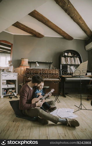 Young father and little daughter playing acoustic guitar in the room at home