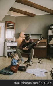 Young father and little daughter playing acoustic guitar in the room at home