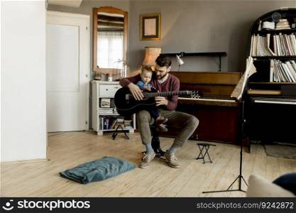 Young father and little daughter playing acoustic guitar in the room at home