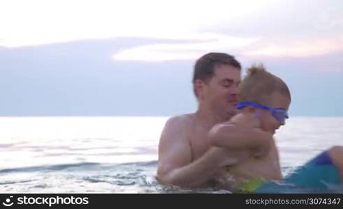 Young father and son in goggles bathing in the sea. Dad spinning chid and then holding him when he flopping about the water