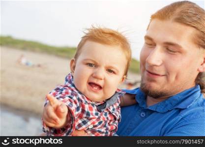 Young father holding his child on the beach. Funny expression, having fun. Son and parent bond