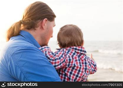 Young father holding his child on the beach having fun together. Son and parent bond