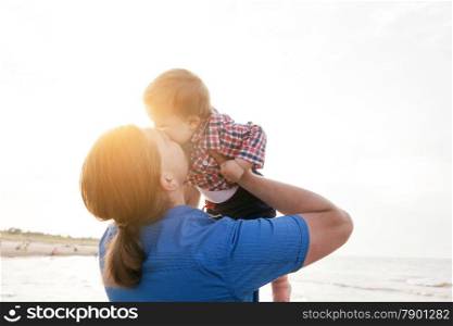 Young father holding his child up in the air on the beach and kissing with love. Son and parent bond