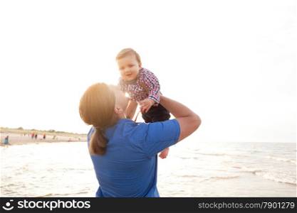 Young father holding his child up in the air on the beach, having fun together. Son and parent bond