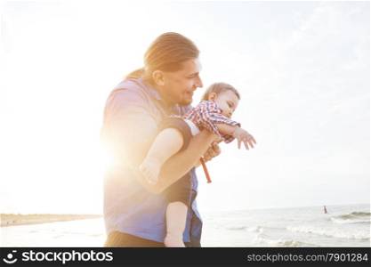 Young father holding his child up in the air on the beach, having fun together. Son and parent bond