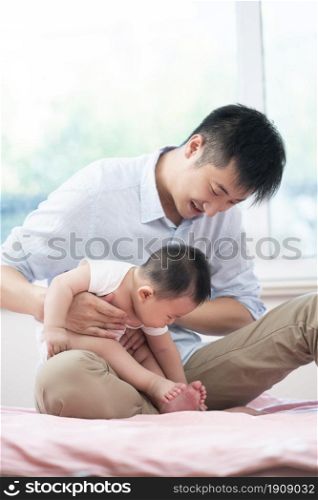 Young father playing with his baby on the bed