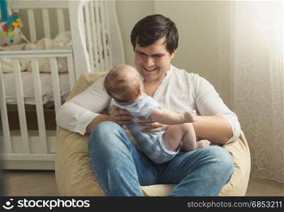Young father sitting in bean bag chair and holding his little baby son