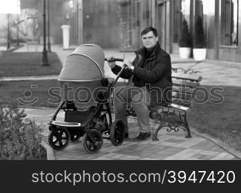 Young father sitting on bench at park with baby stroller