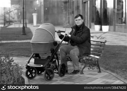 Young father sitting on bench at park with baby stroller