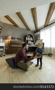 Young father teaching his cute little daughter to play guitar while sitting on the floor in the room