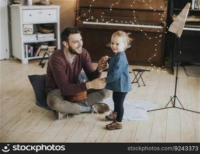Young father teaching his cute little daughter to play guitar while sitting on the floor in the room