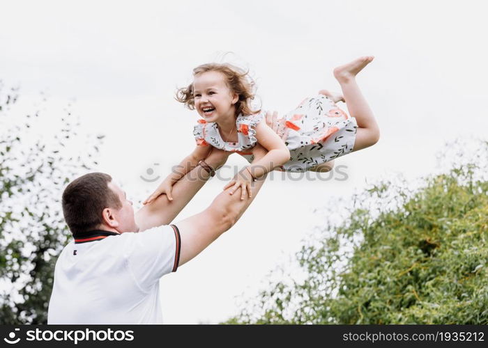 Young father throwing his baby daughter high in the sky in the park in summer day. father&rsquo;s day.. Young father throwing his baby daughter high in the sky in the park in summer day. father&rsquo;s day