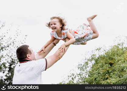 Young father throwing his baby daughter high in the sky in the park in summer day. father&rsquo;s day.. Young father throwing his baby daughter high in the sky in the park in summer day. father&rsquo;s day