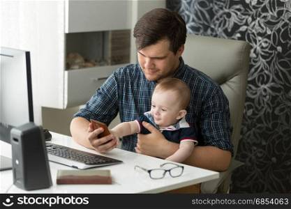 Young father working in office and taking care of baby son