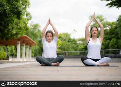 Young female and little girl disciple in the garden there are wooden walkways and a tunnel of fresh green trees. with yoga activities for health
