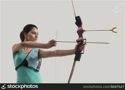 Young female archer with bow and arrow against gray background