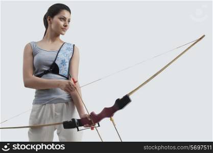 Young female archer with bow and arrow isolated over gray background