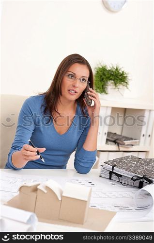 Young female architect working at office holding phone and pen