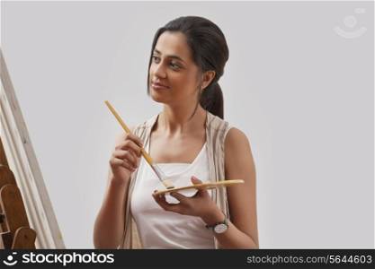 Young female artist painting on canvas isolated over gray background