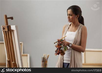 Young female artist wiping hands with cloth while looking at painting
