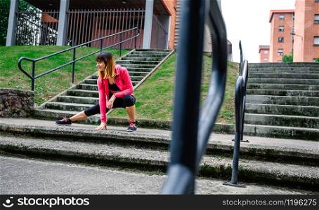 Young female athlete doing stretching on the stairs outdoors. Selective focus on woman in background. Female athlete doing stretching outdoors