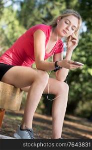 young female athlete in sportswear and headphones sitting on bench