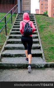 Young female athlete with backpack going up stairs outdoors. Female athlete going up stairs outdoors