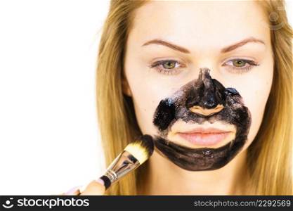 Young female being apply with brush charcoal mask, black detox mud to her face. Girl taking care of oily skin. Beauty treatment. Skincare.. Girl being apply black mask to skin face