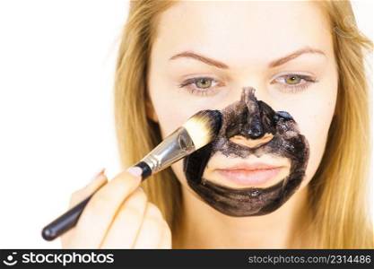 Young female being apply with brush charcoal mask, black detox mud to her face. Girl taking care of oily skin. Beauty treatment. Skincare.. Girl being apply black mask to skin face