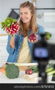 young female blogger on camera screen holding healthy vegetables