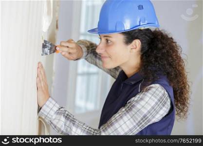 young female builder using scraper to remove wallpaper