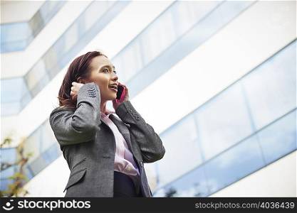 Young female businesswoman talking on smartphone outside office