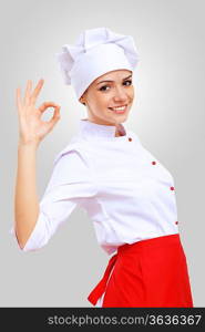 Young female chef in red apron against grey background