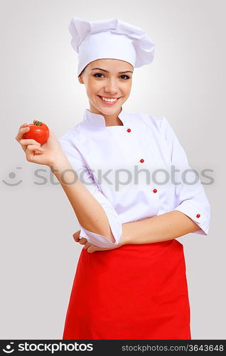 Young female chef in red apron against grey background