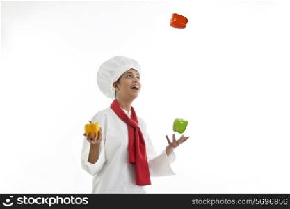Young female chef juggling bell peppers isolated over white background