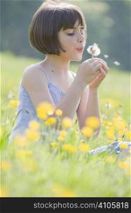 young female child sitting in field of buttercups blowing a dandelion