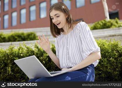 Young Female College Student OR Office Worker With Laptop Having Video Chat Outdoors On College Campus
