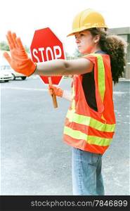 Young female construction apprentice holding a stop sign and directing traffic.