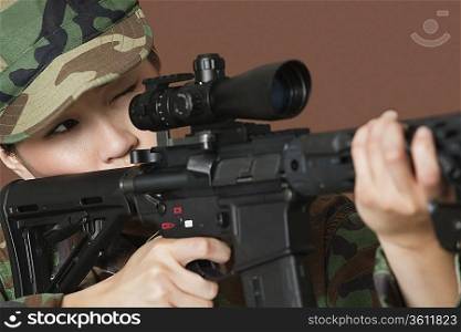 Young female Corps soldier aiming M4 assault rifle over brown background