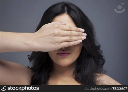 Young female covering eyes her with hand over colored background
