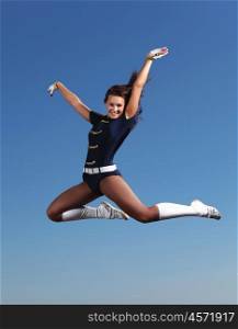 Young female dancer against white background. Young cheerleader in green costume jumping against blue sky