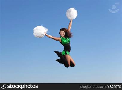 Young female dancer against white background. Young cheerleader in green costume jumping against blue sky