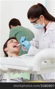 Young female dentist working on patient&rsquo;s teeth with assistant in the background