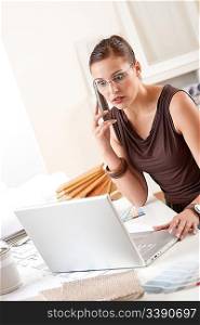Young female designer on the phone at office with laptop and color swatch