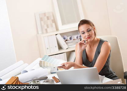 Young female designer working at office with laptop and color swatch