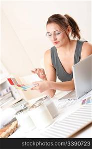 Young female designer working at office with laptop and color swatch