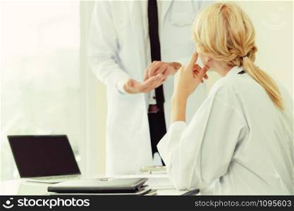 Young female doctor at hospital office having conversation talking with another male doctor standing beside the table. Concept of medical healthcare professional team.