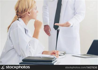 Young female doctor at hospital office having conversation talking with another male doctor standing beside the table. Concept of medical healthcare professional team.. Female doctor at hospital talking to her partner.