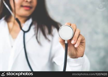 Young female doctor at hospital pointing stethoscope at blank space. Selective focus at doctors hand. Medical healthcare concept.. Doctor pointing stethoscope at blank space.