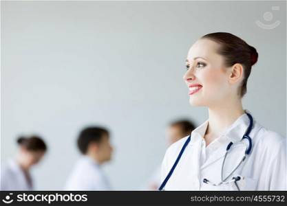 Young female doctor. Attractive female doctor in white uniform with colleagues at background